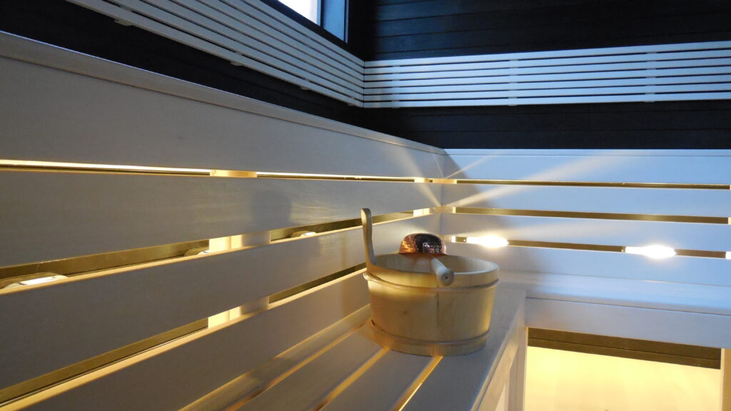 Sauna with white benches, warm LED lighting and a wooden bucket