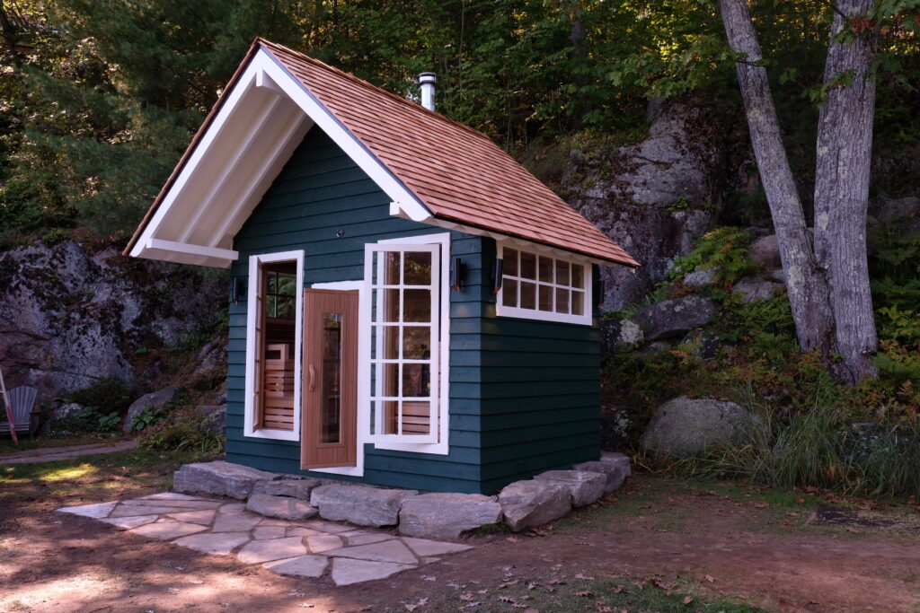 Lakeside cottage-style outdoor sauna with a cedar shingle roof