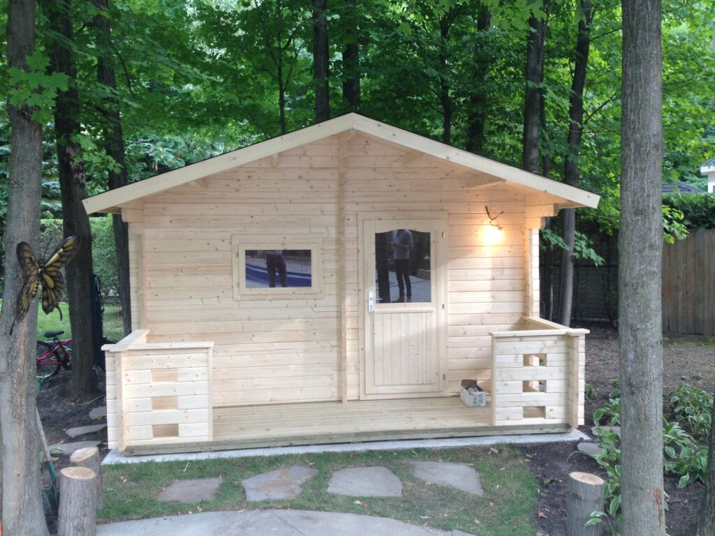Log cabin outdoor sauna with porch lights in a wooded backyard